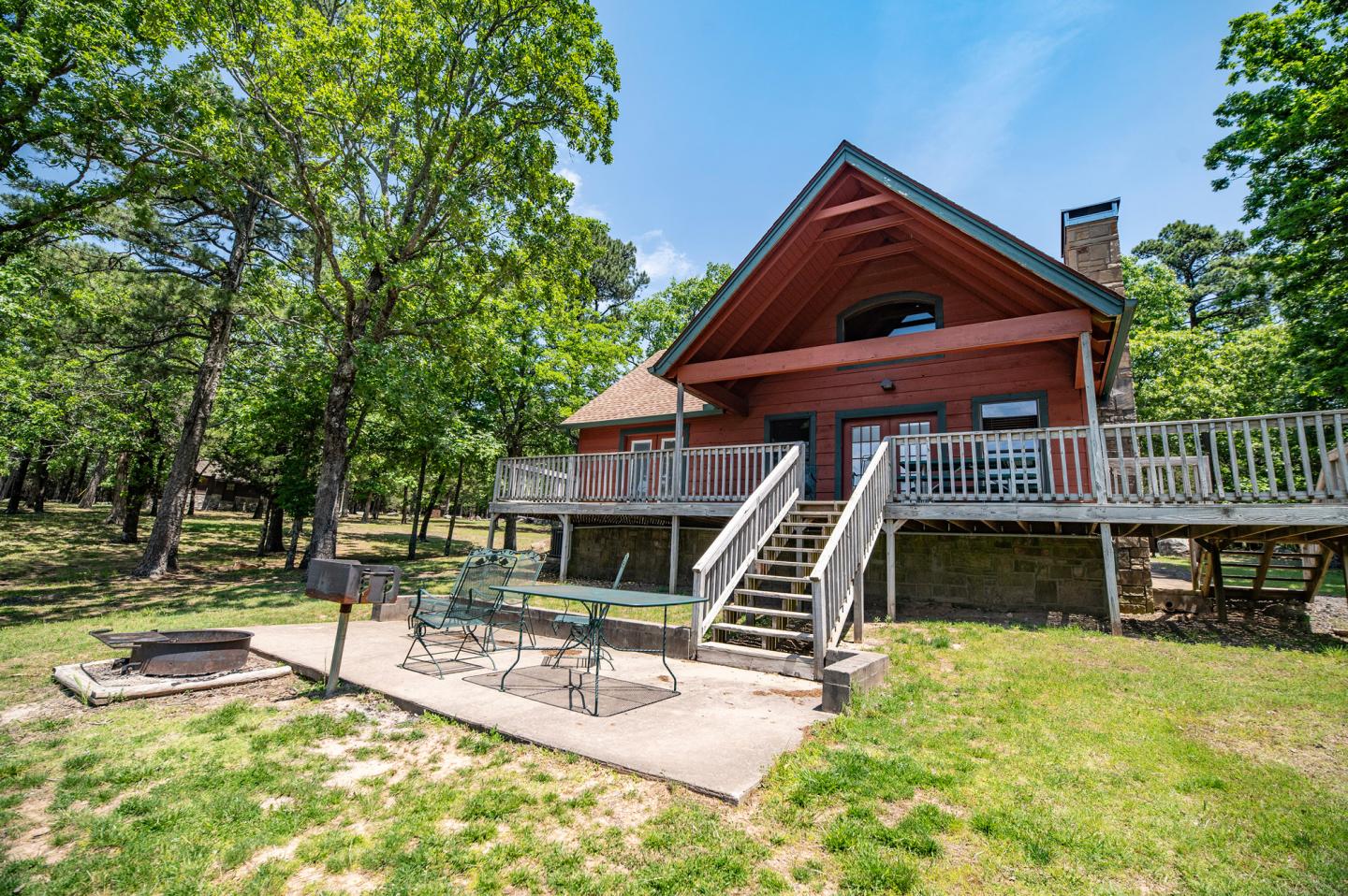 A-frame cabin with a wooden deck in a wooded area on a sunny day.