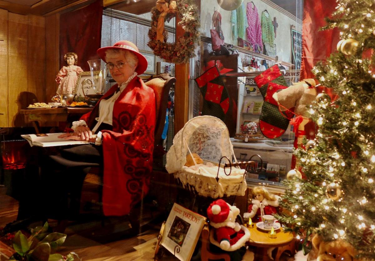 Cozy holiday display with festive decor and mannequin in red outfit, next to a Christmas tree.