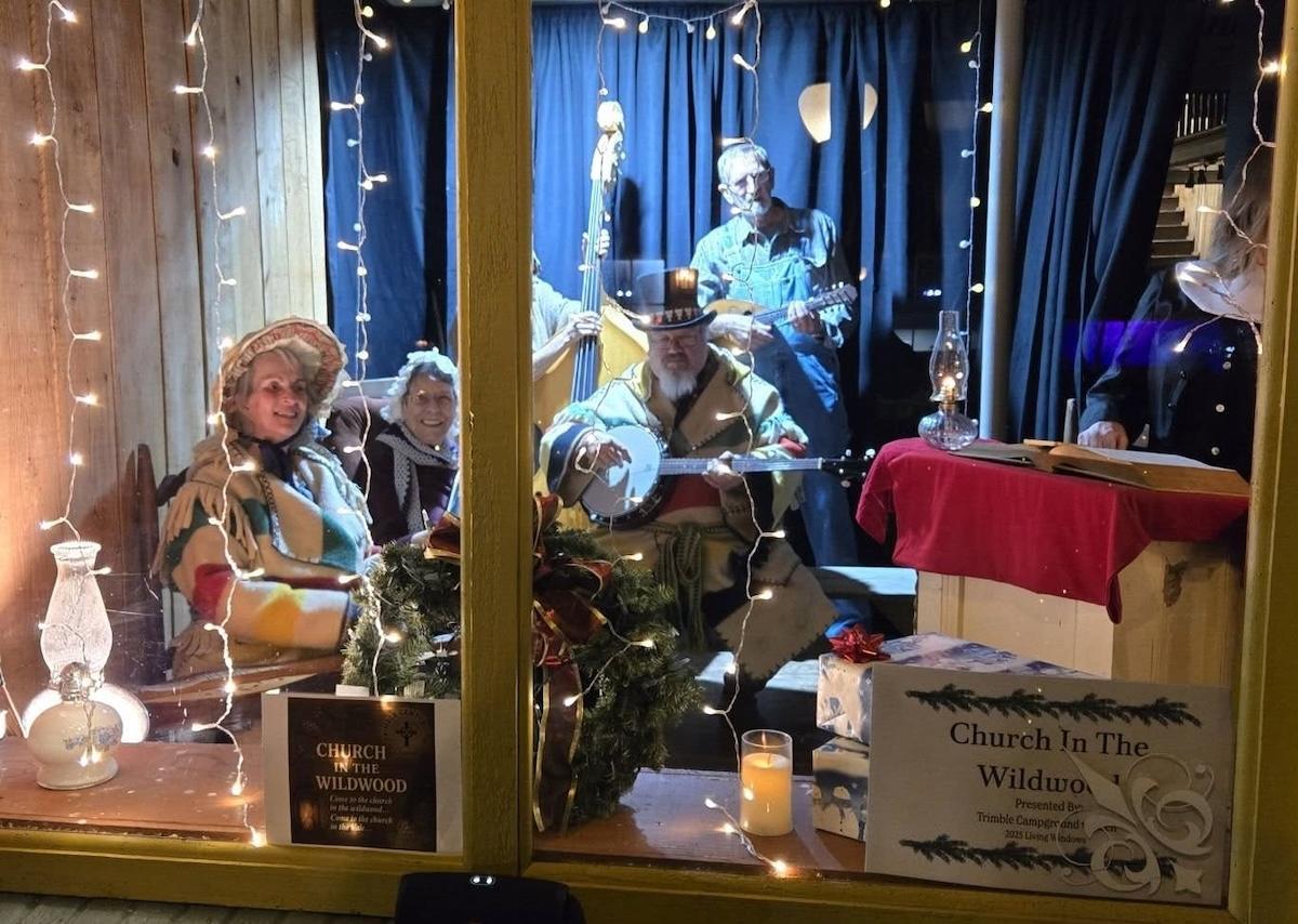 Victorian-dressed musicians performing in a festively lit window display.