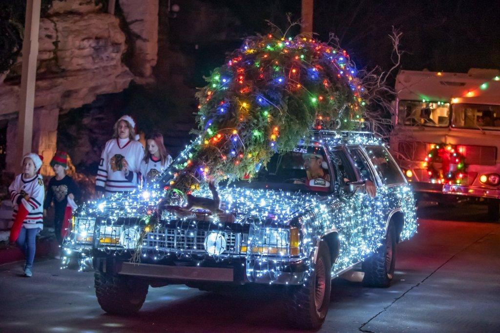 A car covered in Christmas lights with a decorated tree on top.