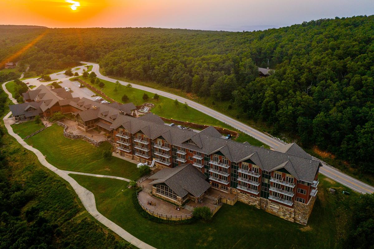 Sunset over a large lodge surrounded by lush green trees and winding paths.