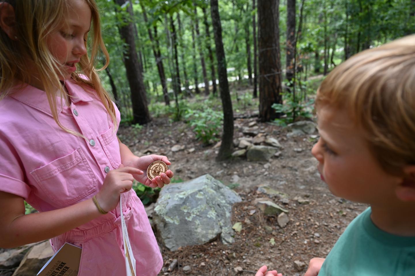 Kids examining Explorer badge in a forest clearing.