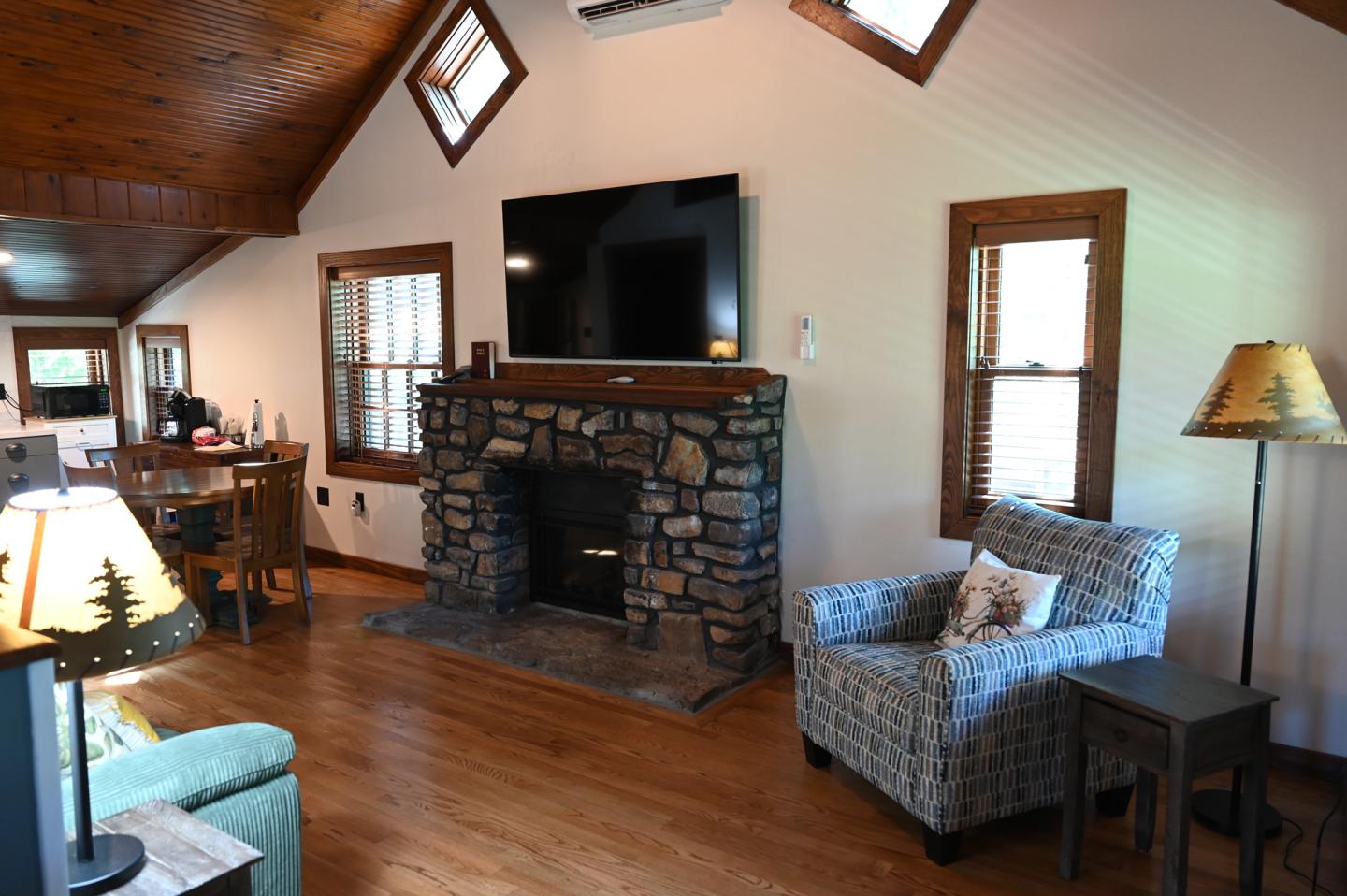 Cozy living room with stone fireplace and large TV, wooden ceiling, and comfortable chairs.