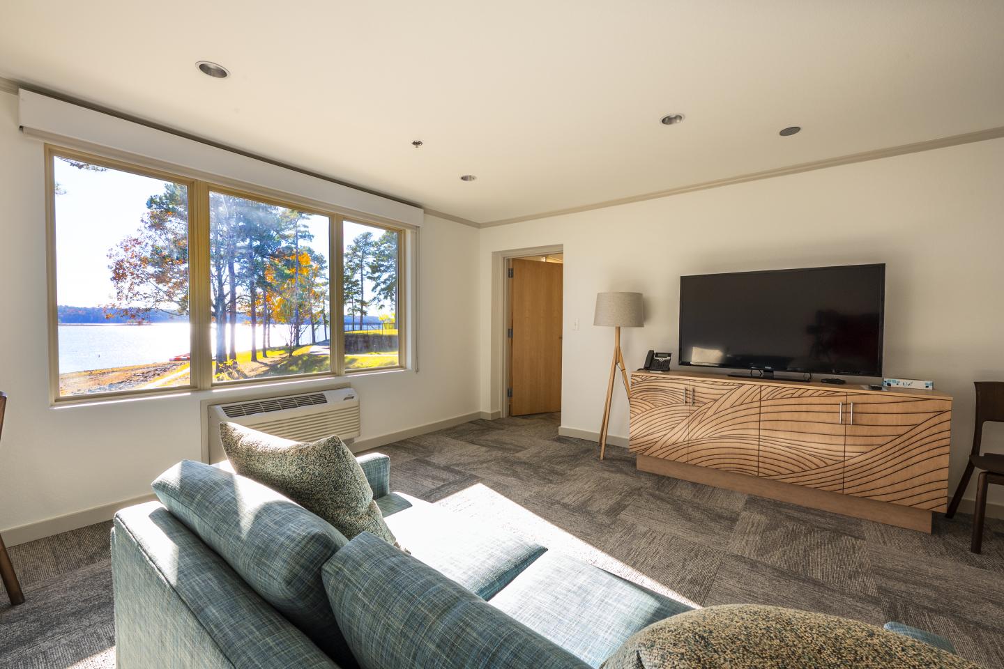 Living room with a large window view of trees, a sofa, TV, and wooden cabinet.