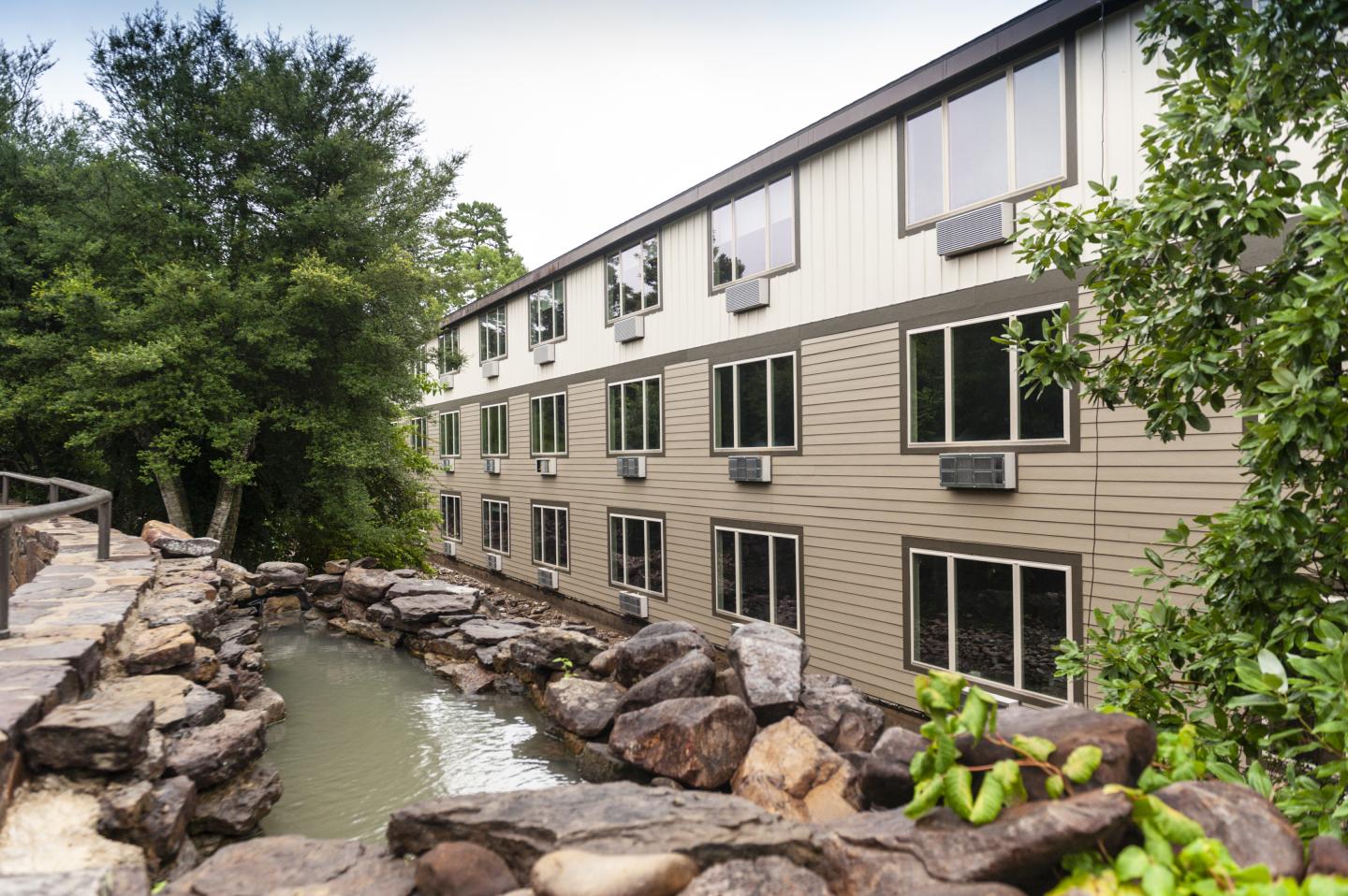 Stream beside a three-story building, surrounded by rocks and trees.
