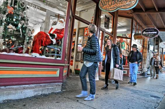 Shoppers in winter clothes pass a storefront with a Santa display.