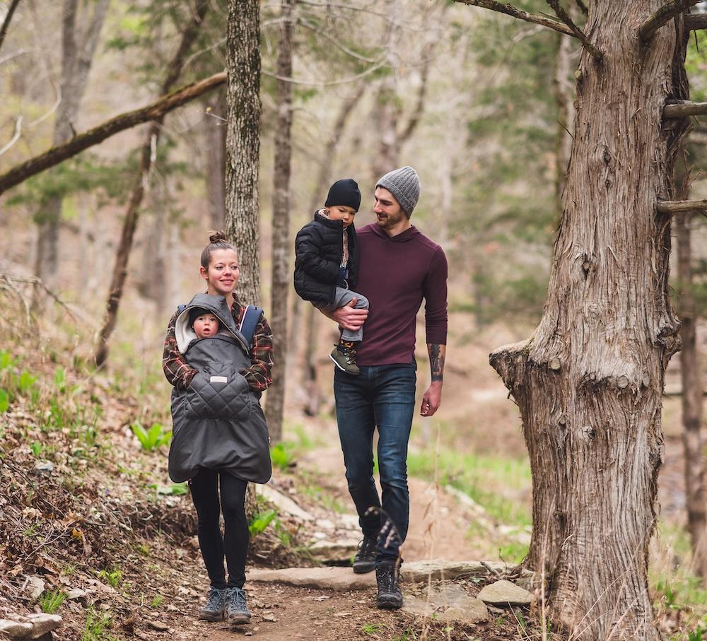 Family walking on a forest path, parents carry young children, smiling.