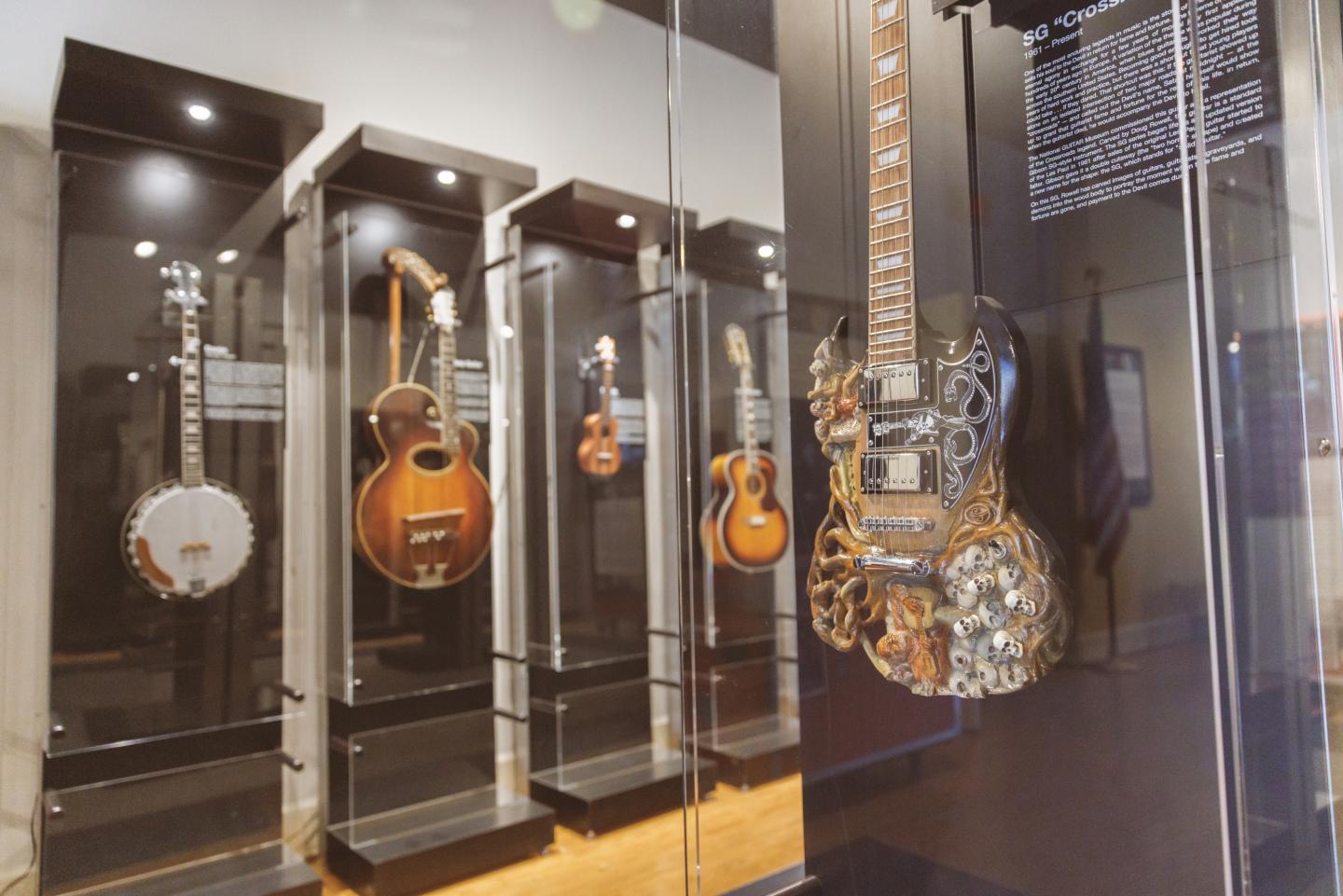 Guitars and banjo displayed in a museum exhibit with glass cases.