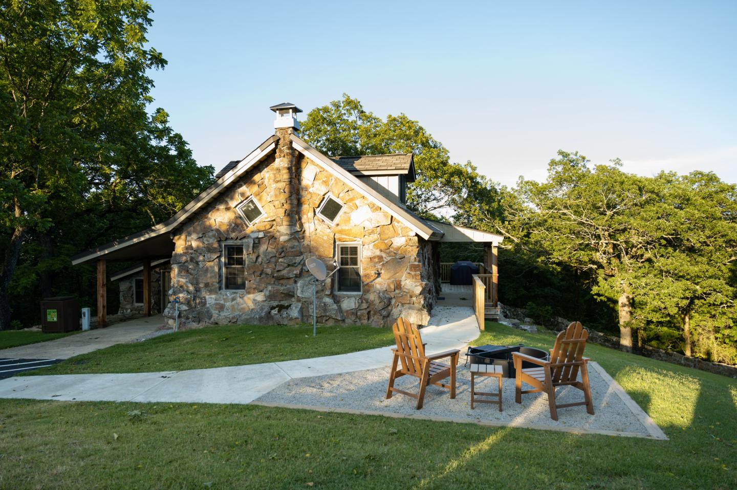 Stone cabin in a wooded area with chairs on a patio.