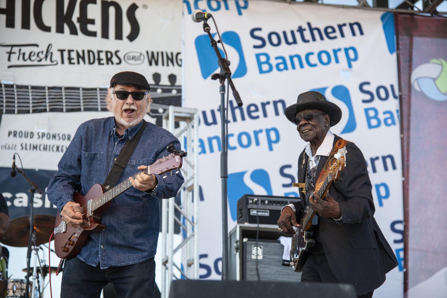 Musicians playing guitars on stage at an outdoor event.