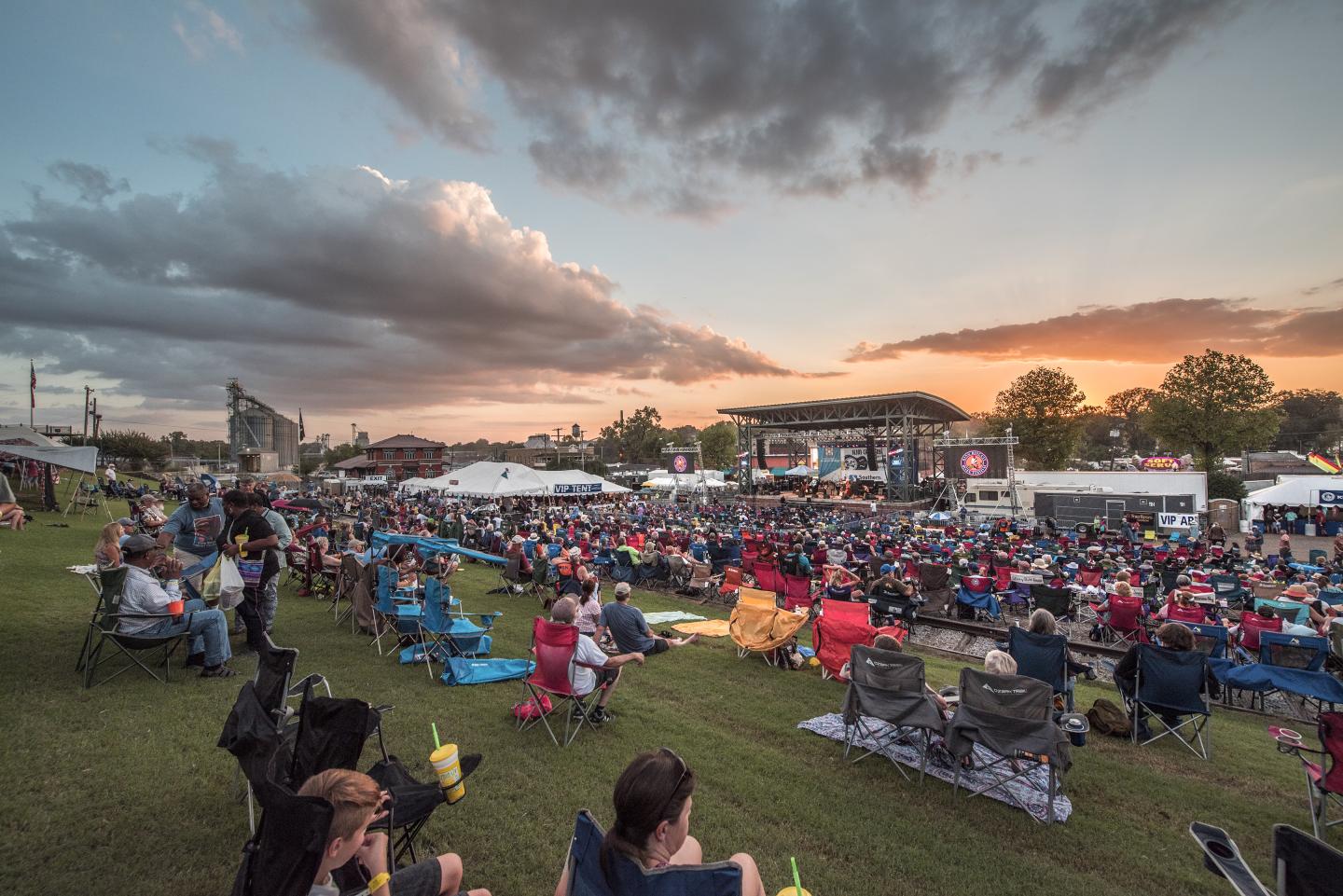 Outdoor concert at sunset with a crowd seated on grass.