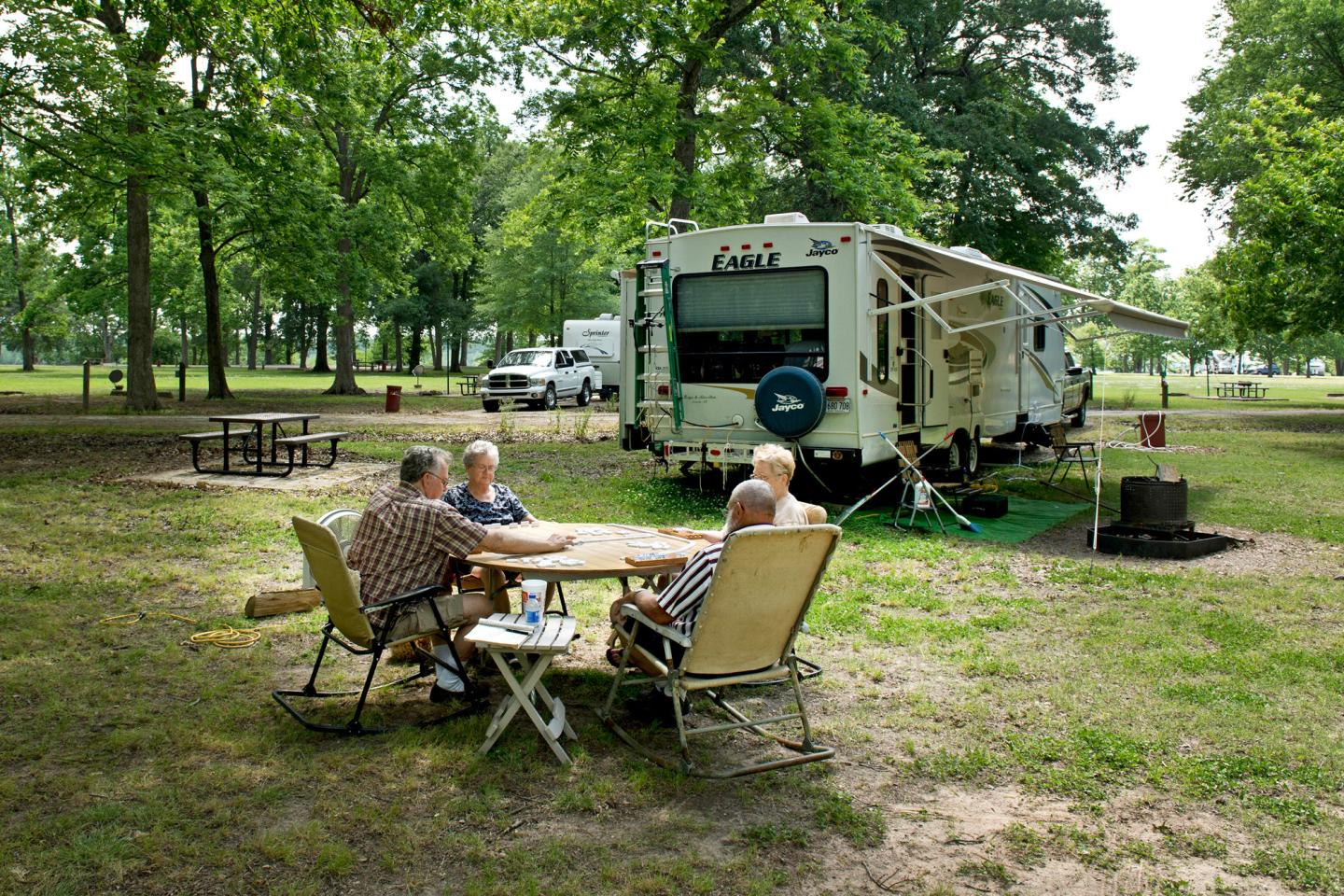 RV parked in a grassy area with four people seated at a table nearby.