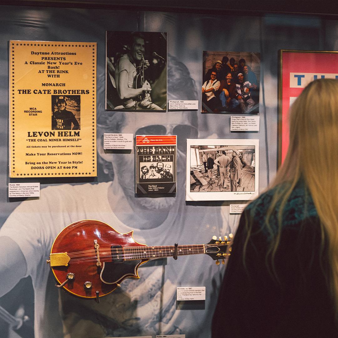 Exhibit wall with photographs, a guitar, and a person viewing them.