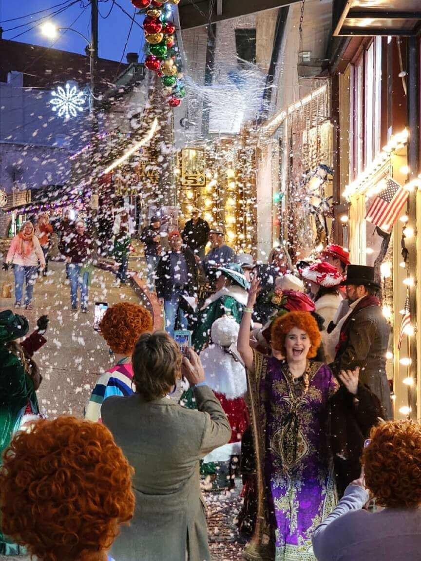 Street celebration with festive lights and people in colorful costumes, confetti falling.
