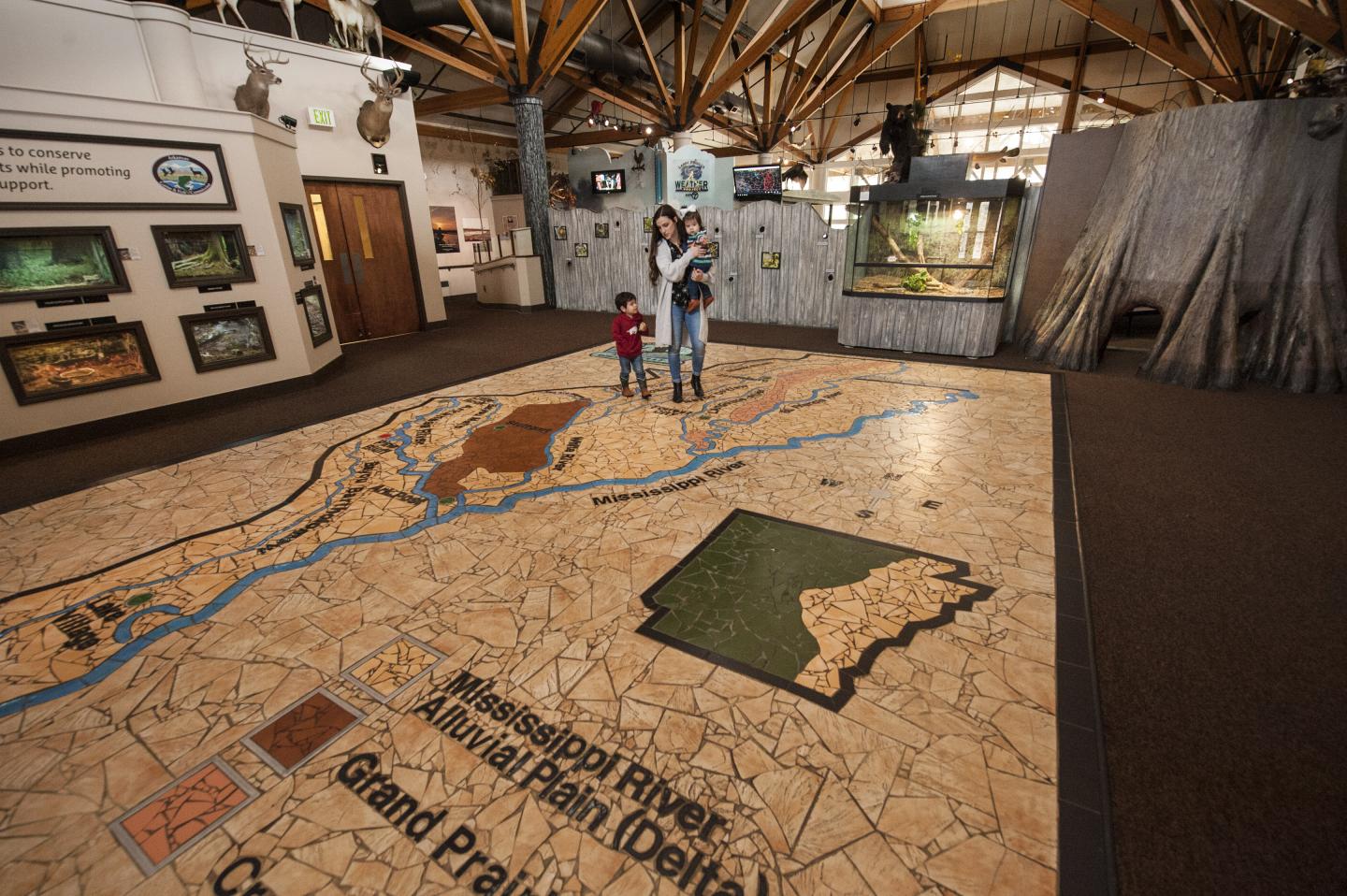 Museum interior with large floor map, woman and child observing.