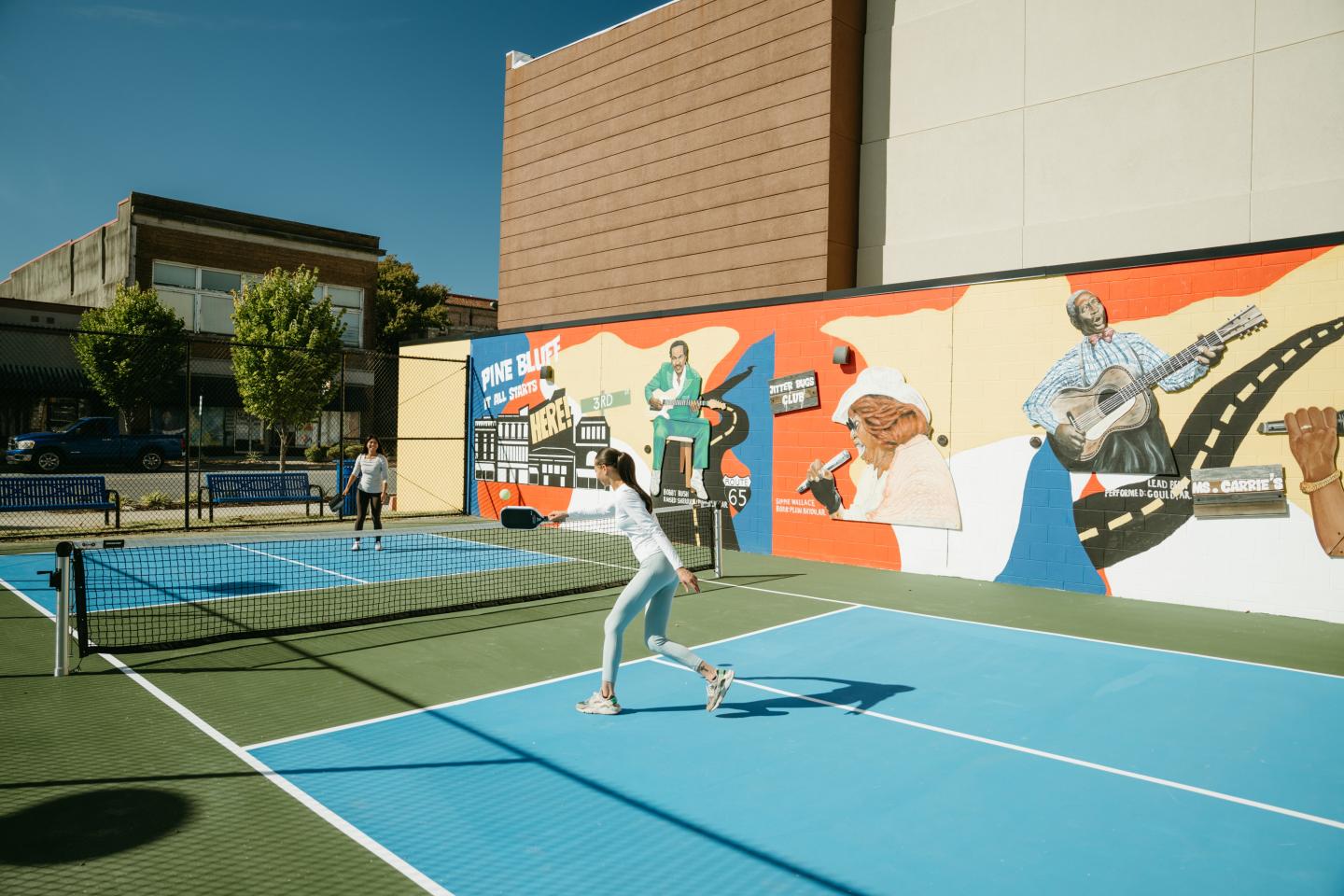 Tennis players on a blue court near a colorful mural.