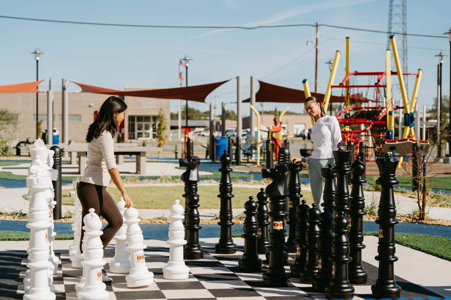 Two people playing giant chess outdoors in a sunny park.