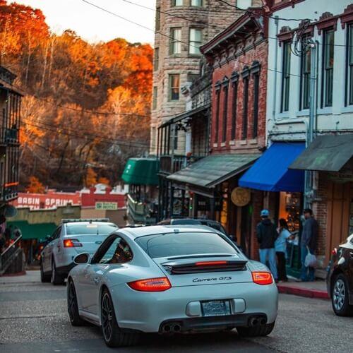 A white sports car on a bustling street with autumn trees in the background.