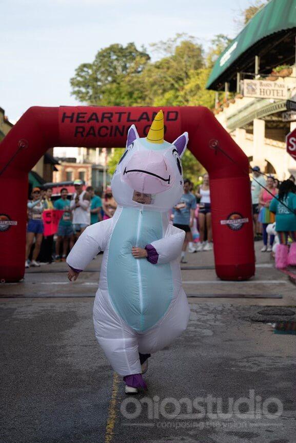 Unicorn costume runner in a race under red archway.