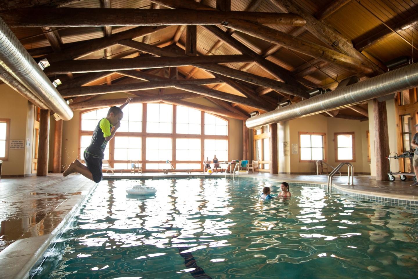 Indoor pool with wooden beams, kids swimming, and a child jumping in.
