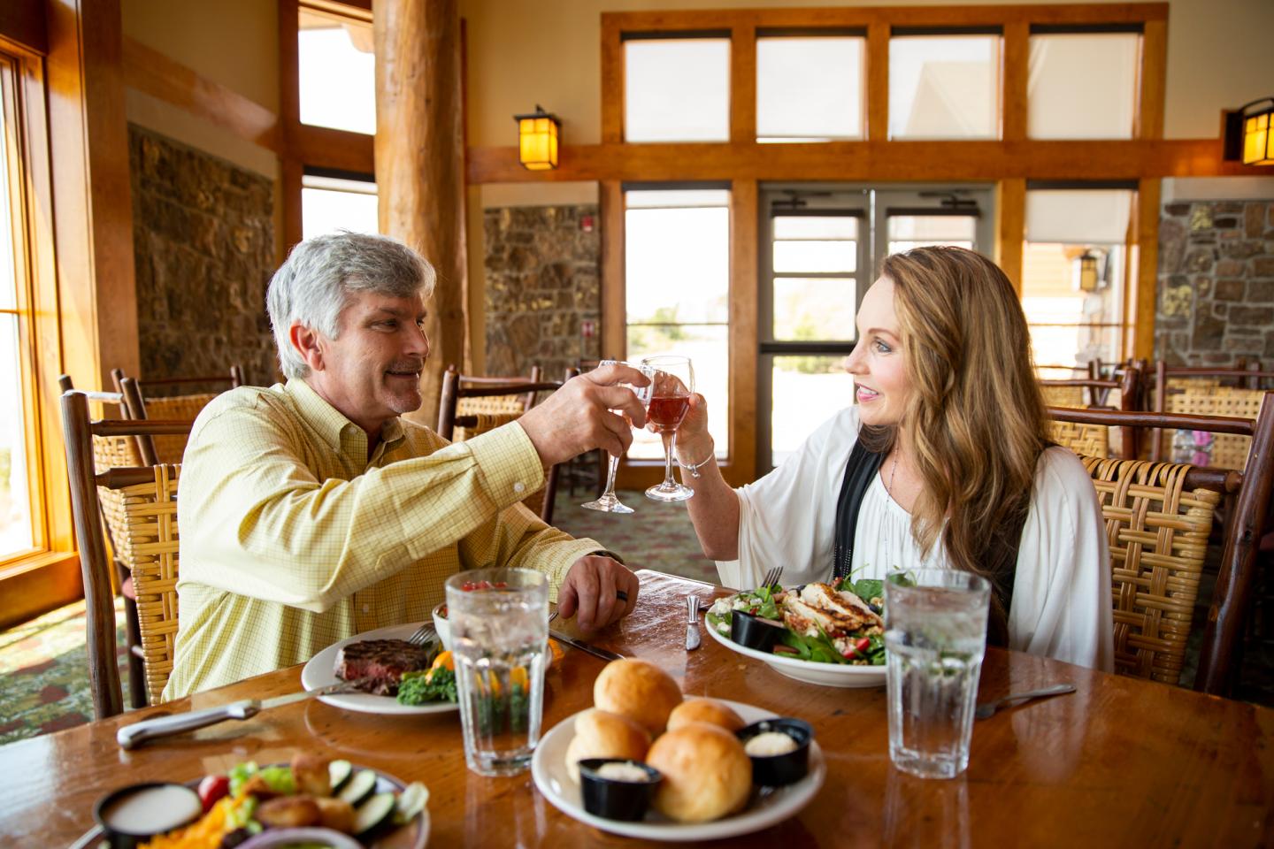 Couple toasting drinks at a restaurant table with meals.