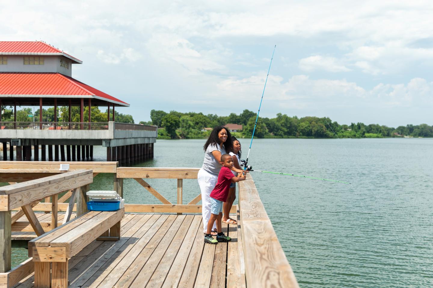 Mother and child fishing on a pier under a cloudy sky.