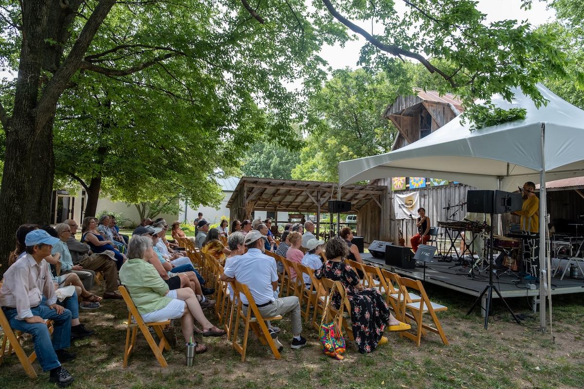 Outdoor gathering with people seated, watching a band under a white tent.