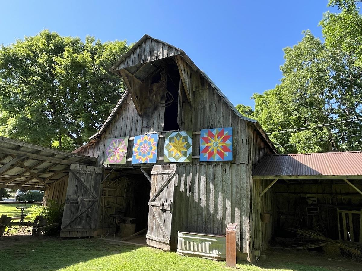 Wooden barn with colorful quilt patterns on sunny day.