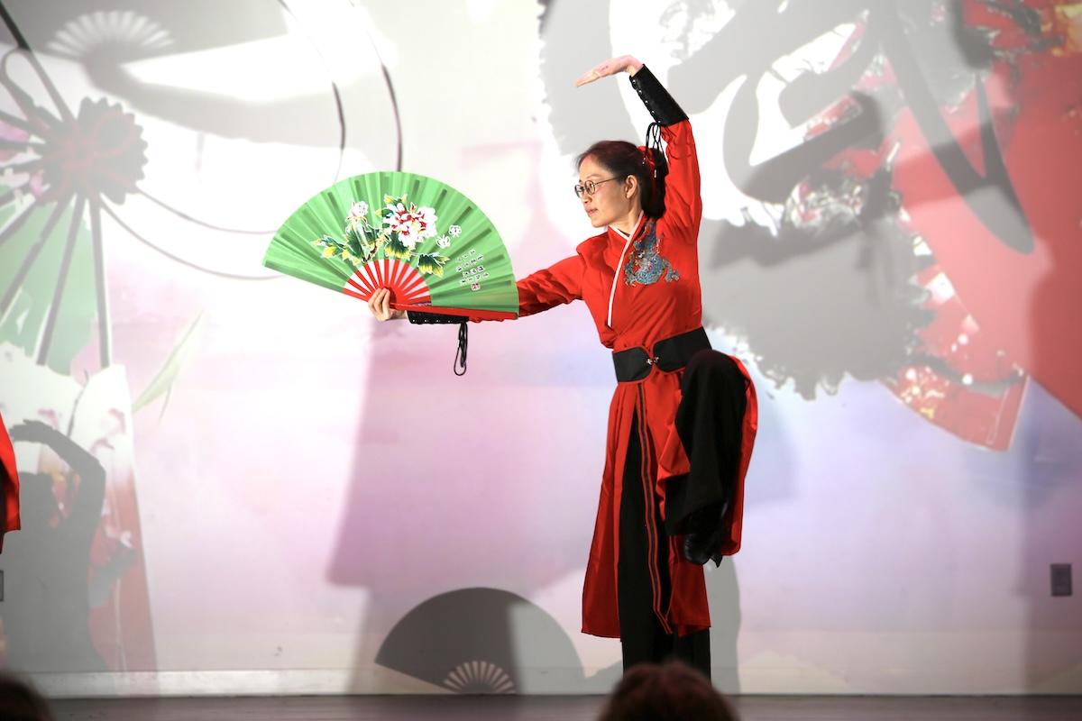 Person in red costume performing a dance with a green fan on a colorful stage.