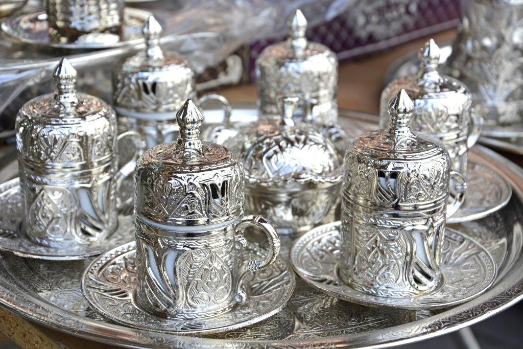 Ornate silver teacups with lids on a matching tray.