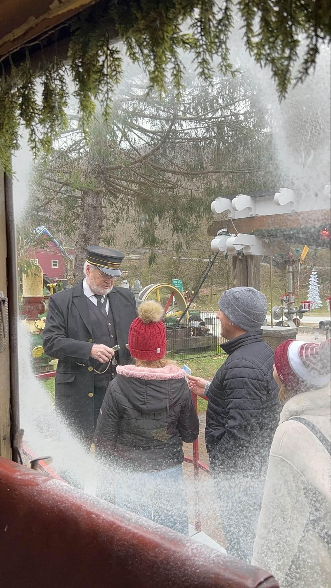 Conductor collecting tickets from passengers wearing winter coats and hats, viewed through a frosted window.