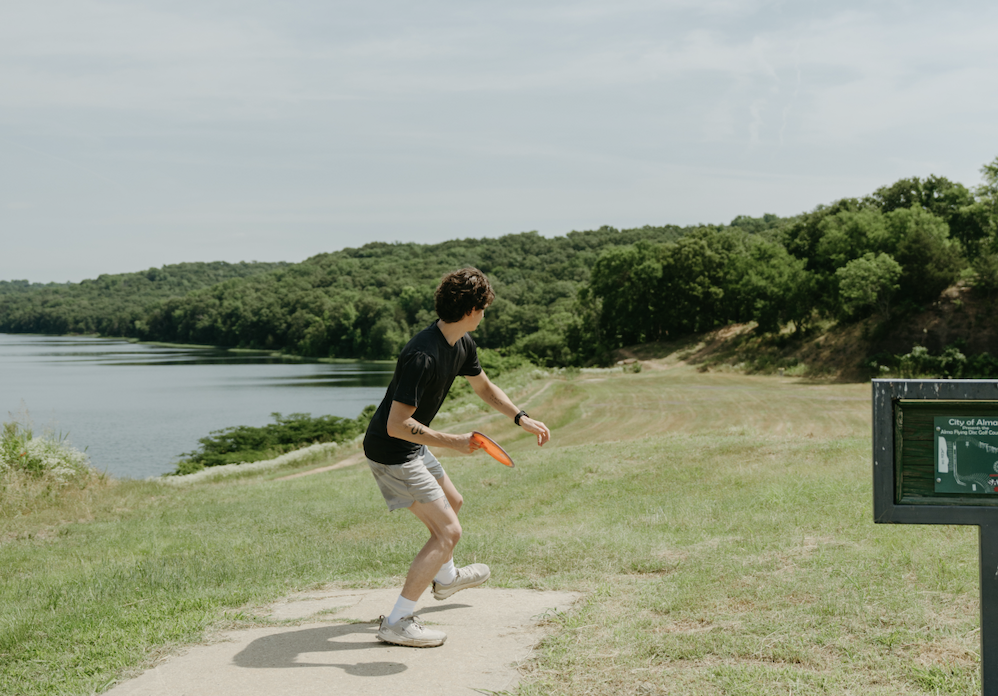 Person playing disc golf near a lake on a sunny day.