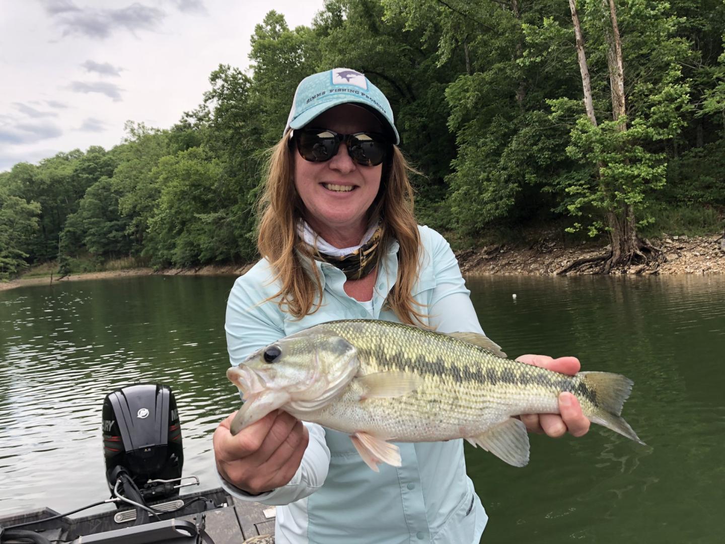 Person holding a fish on a boat, surrounded by trees and water.