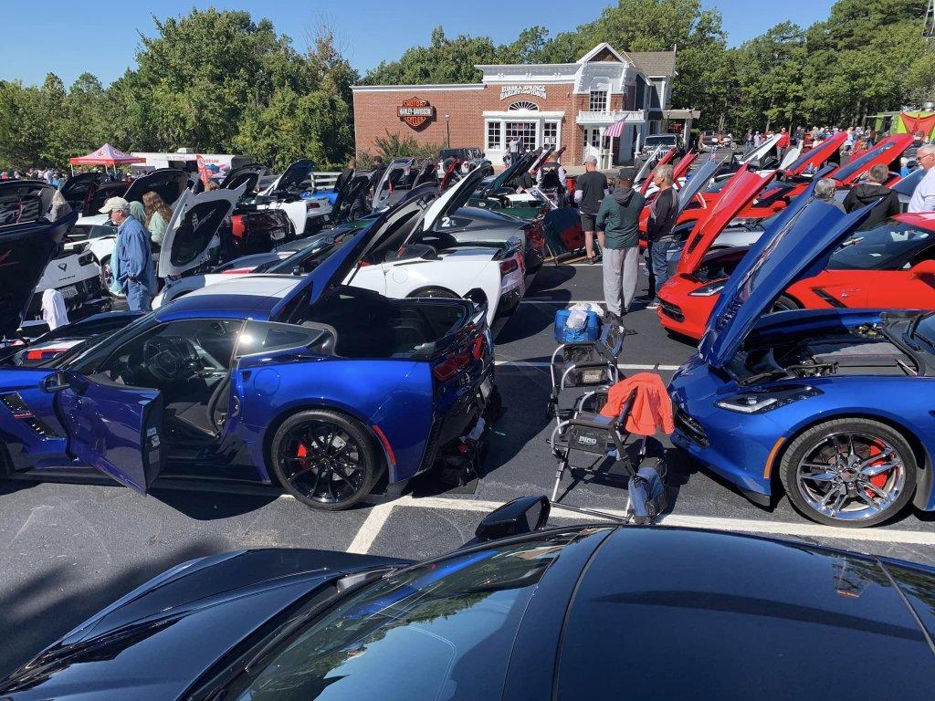 Cars with open hoods at a car show in a parking lot.