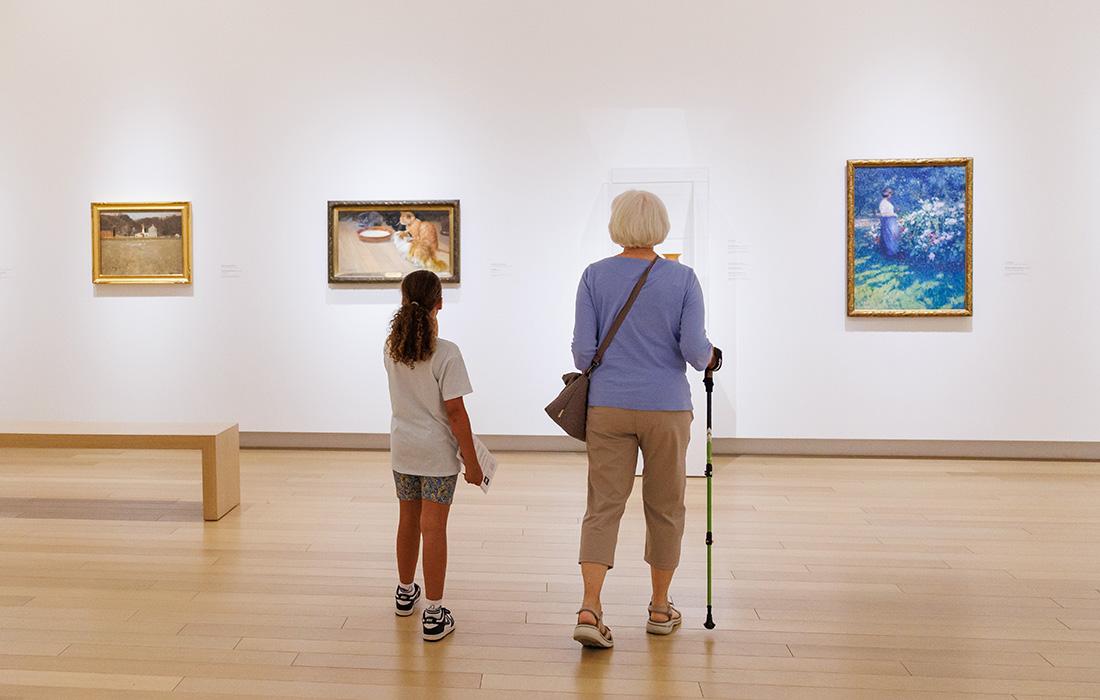 Two people view paintings in a bright art gallery.