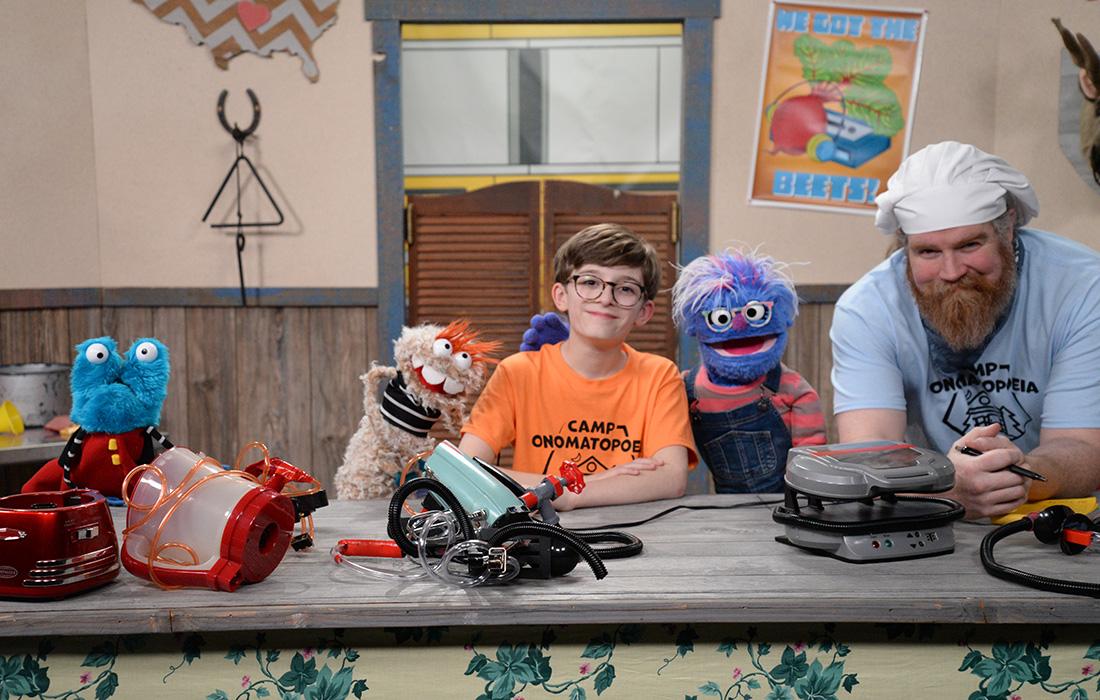 Kids and puppets with electrical tools at a workshop table.