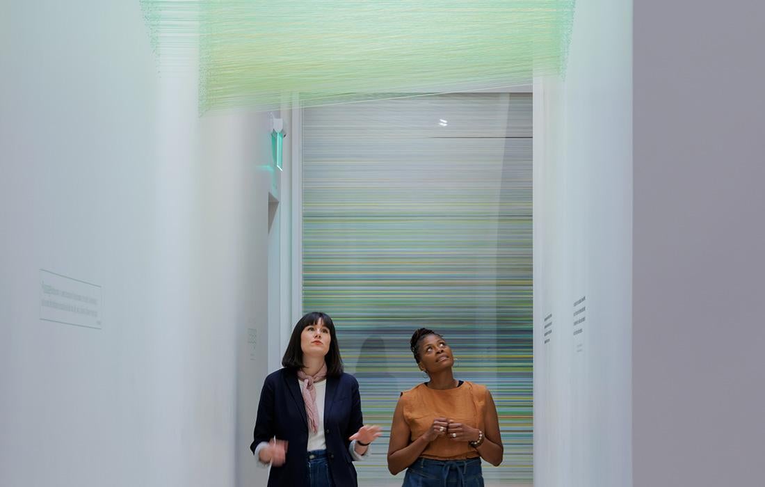 Two people look up at a green art installation in a modern gallery.