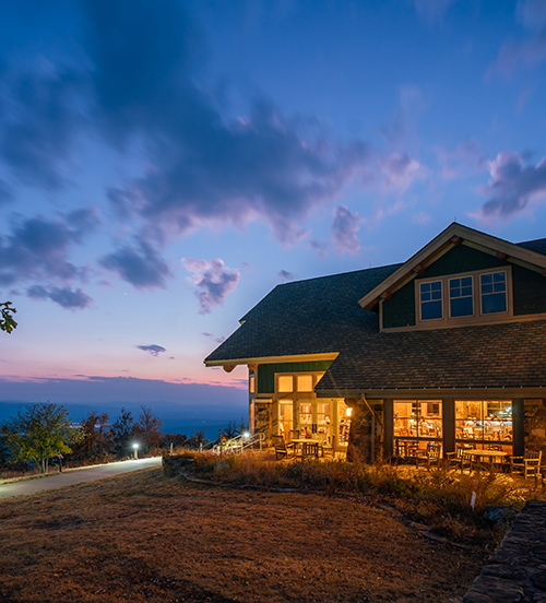 House at sunset with lit windows, surrounded by scenic landscape.