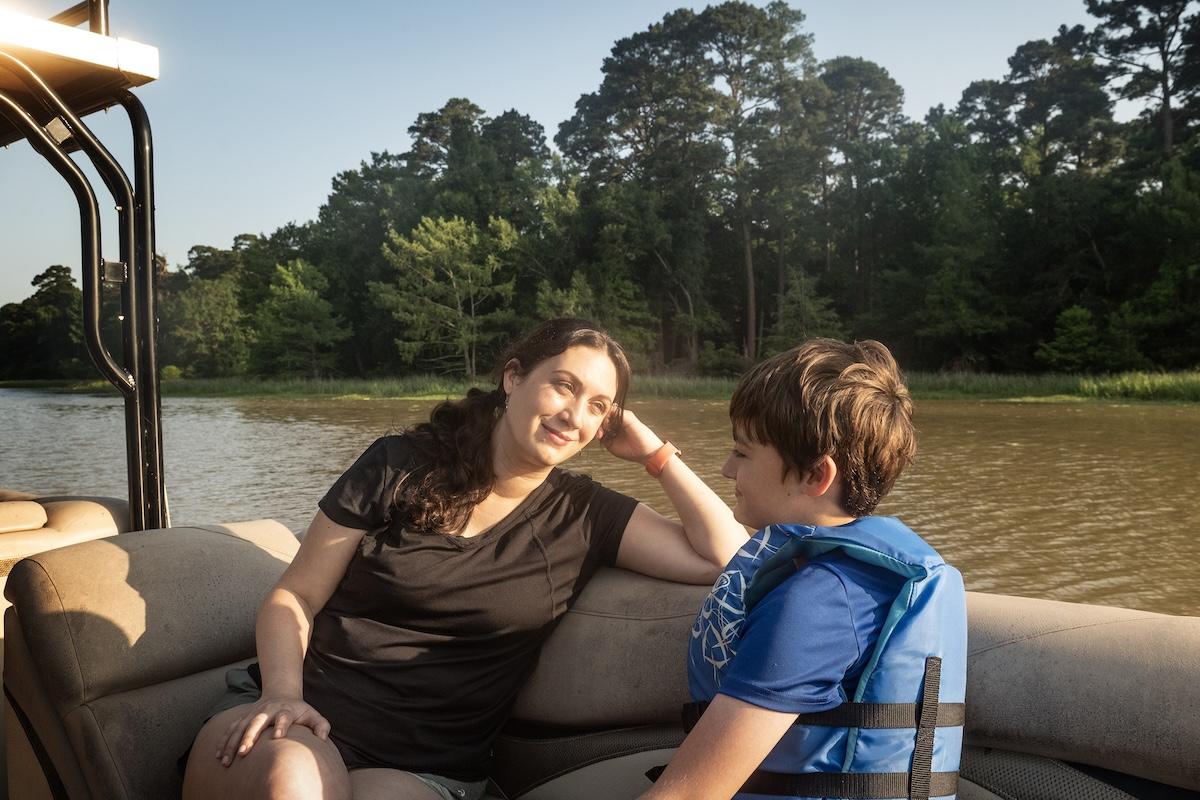 Woman and child smiling on a boat, surrounded by water and trees.