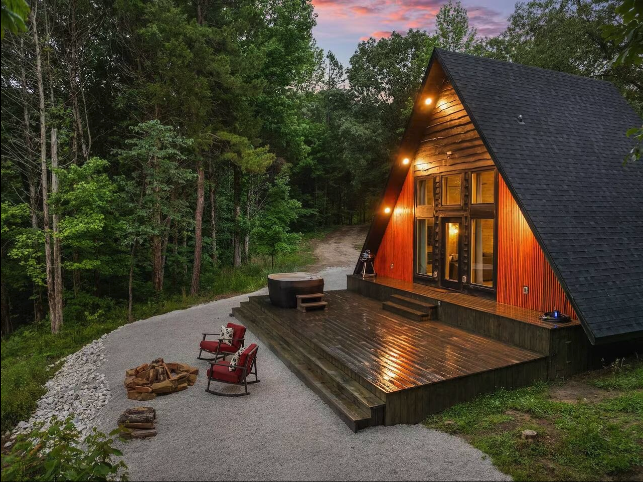 A-frame cabin at dusk with lit patio, surrounded by trees.