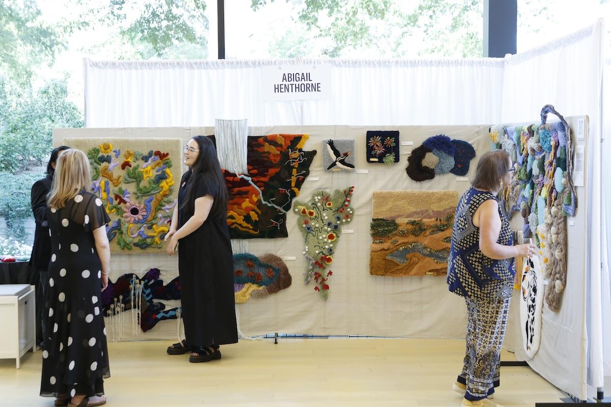 Women admiring colorful textile art on a white display wall.