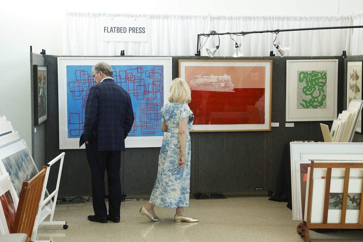 Art exhibit with two people viewing colorful framed prints.