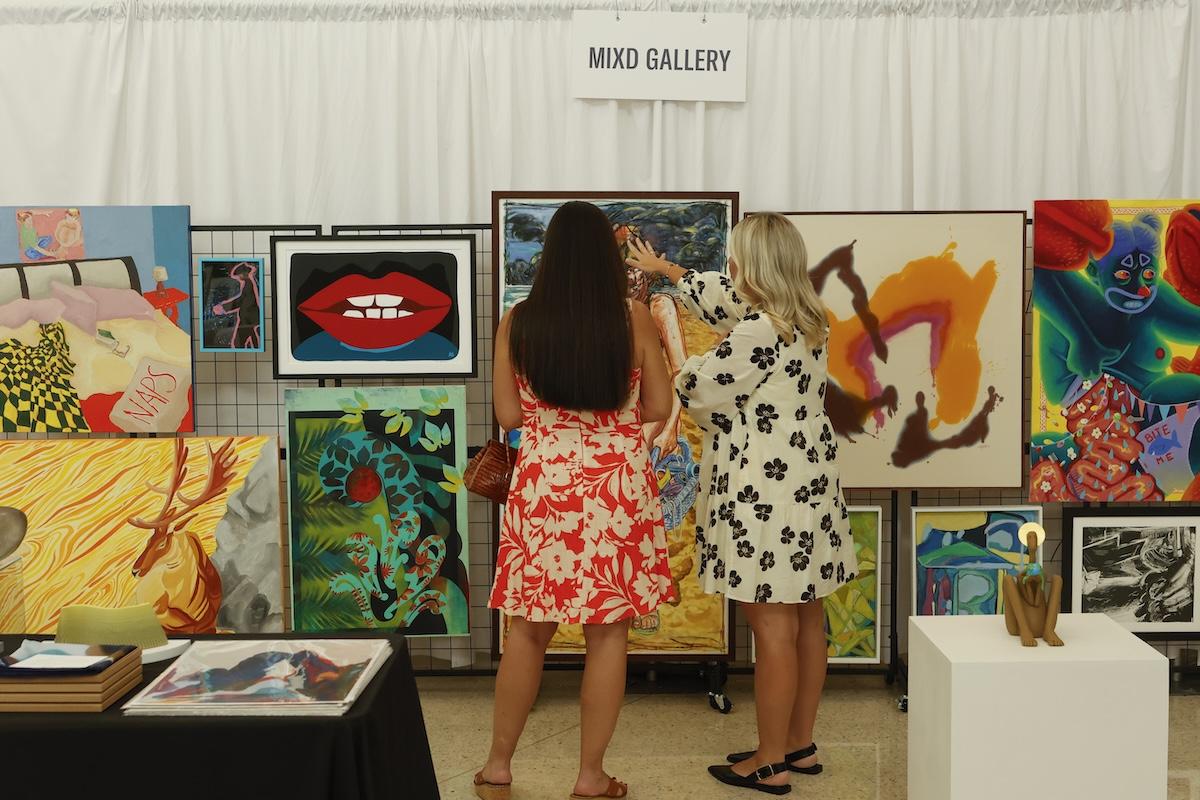 Two women in a gallery, observing colorful artwork.