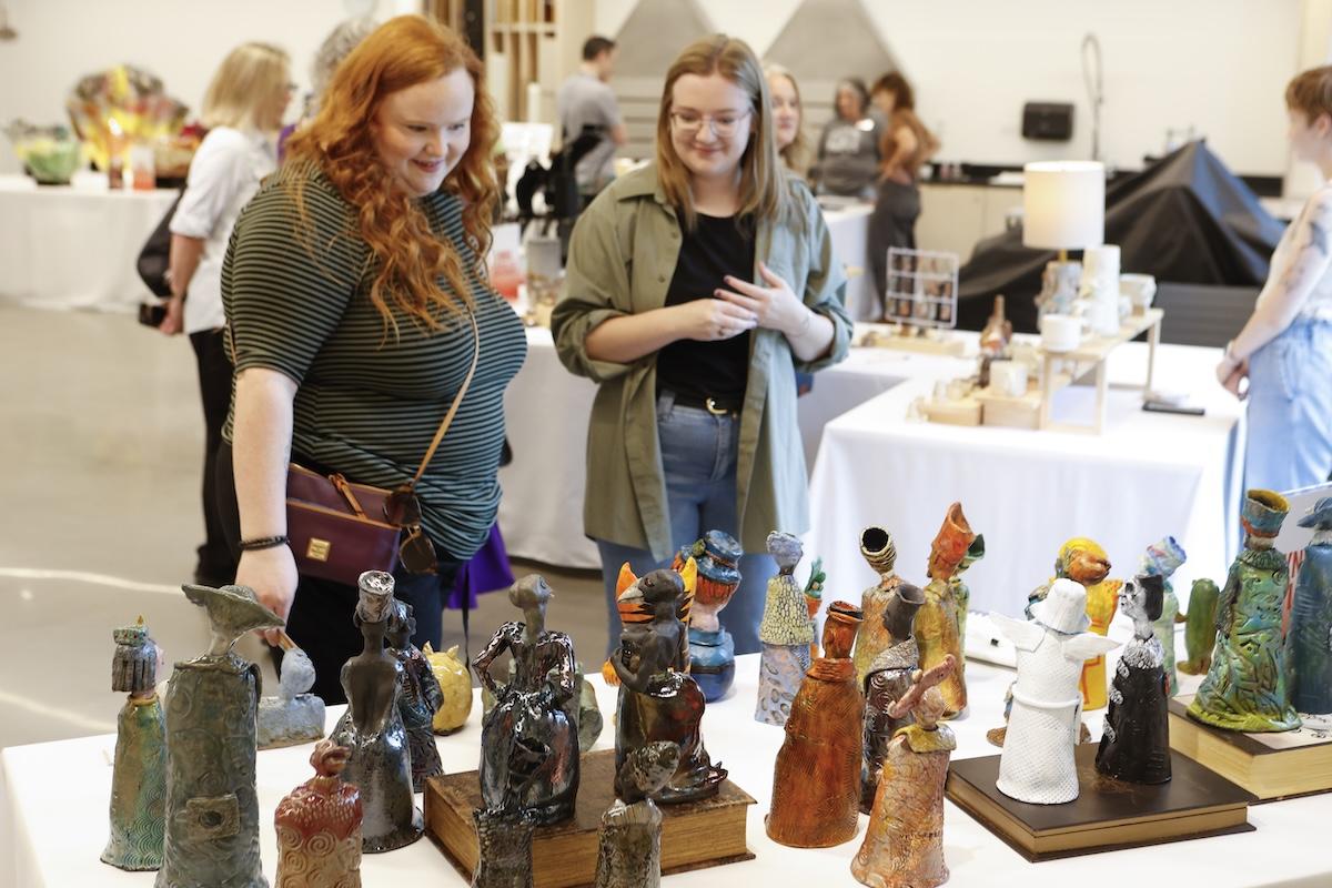 Two women admiring ceramic sculptures on display in a gallery setting.