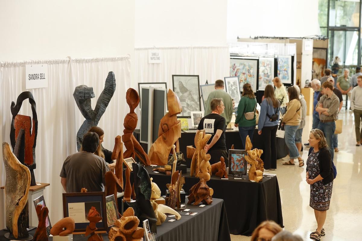 Art gallery with sculptures and paintings, visitors browse exhibits.