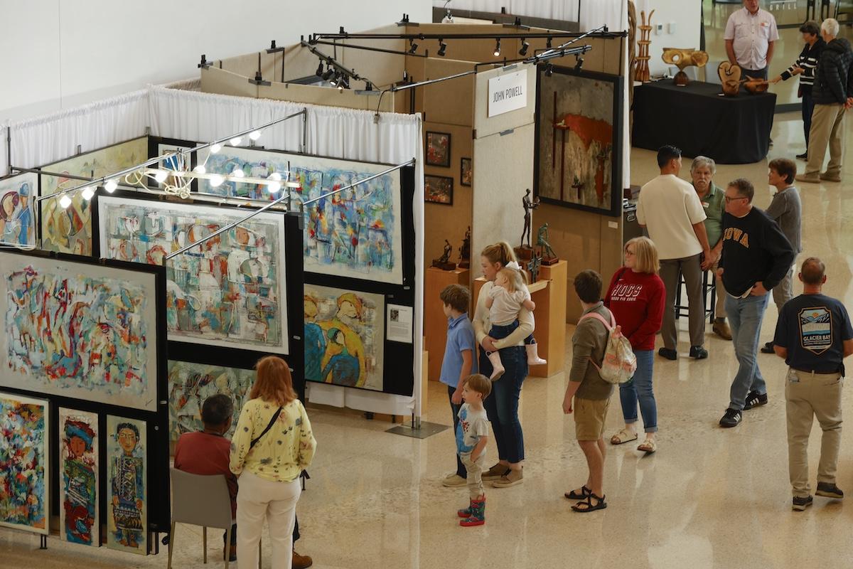 Art exhibit with people viewing colorful paintings in a gallery setting.