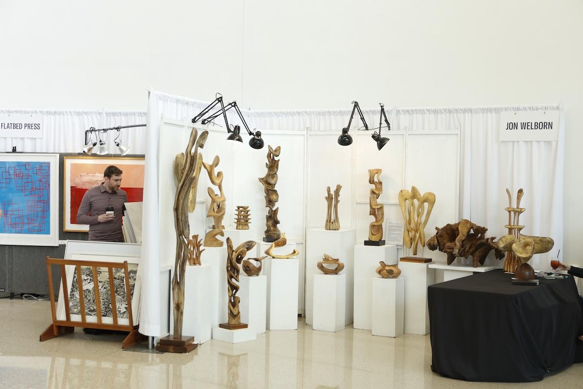Art exhibition with wooden sculptures and a person behind a desk.