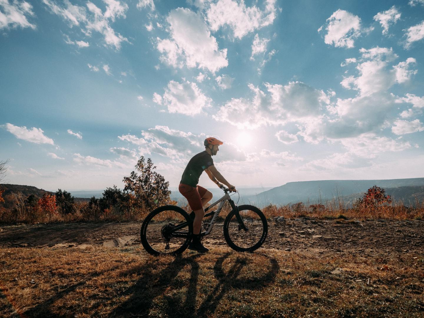 Cyclist riding on a trail at sunset with a vast sky and distant hills.