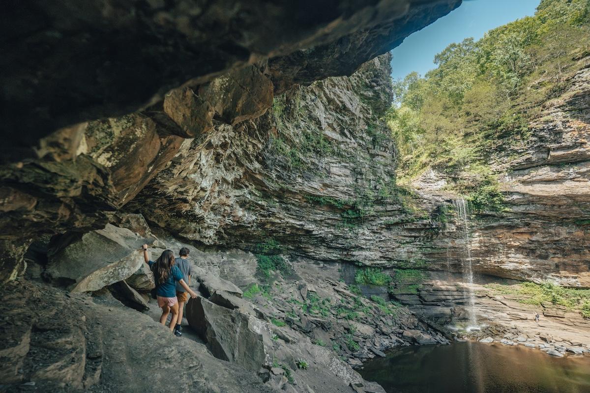 Rocky cliffside with hikers and waterfall in the background.