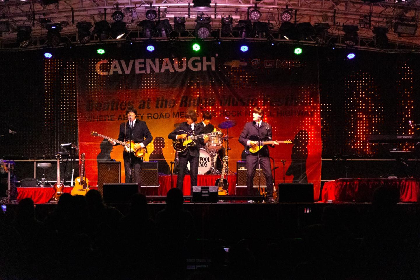 Live band performing on a stage with colorful lighting and a backdrop.